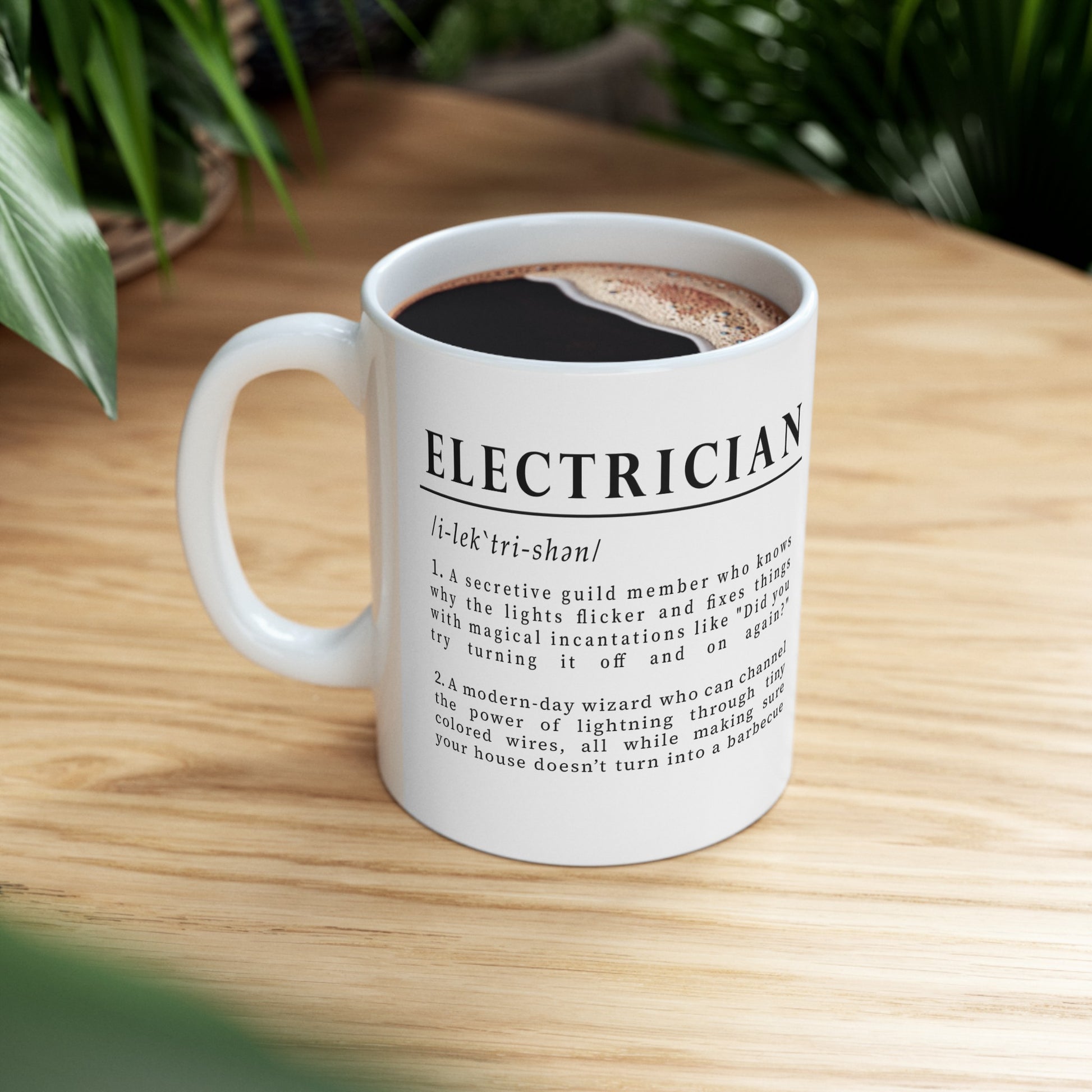 The image shows a white ceramic mug with a humorous definition of 'Electrician' in bold black font. The text describes an electrician as both a secretive guild member and a modern-day wizard of electricity, adding a playful twist to the profession. 