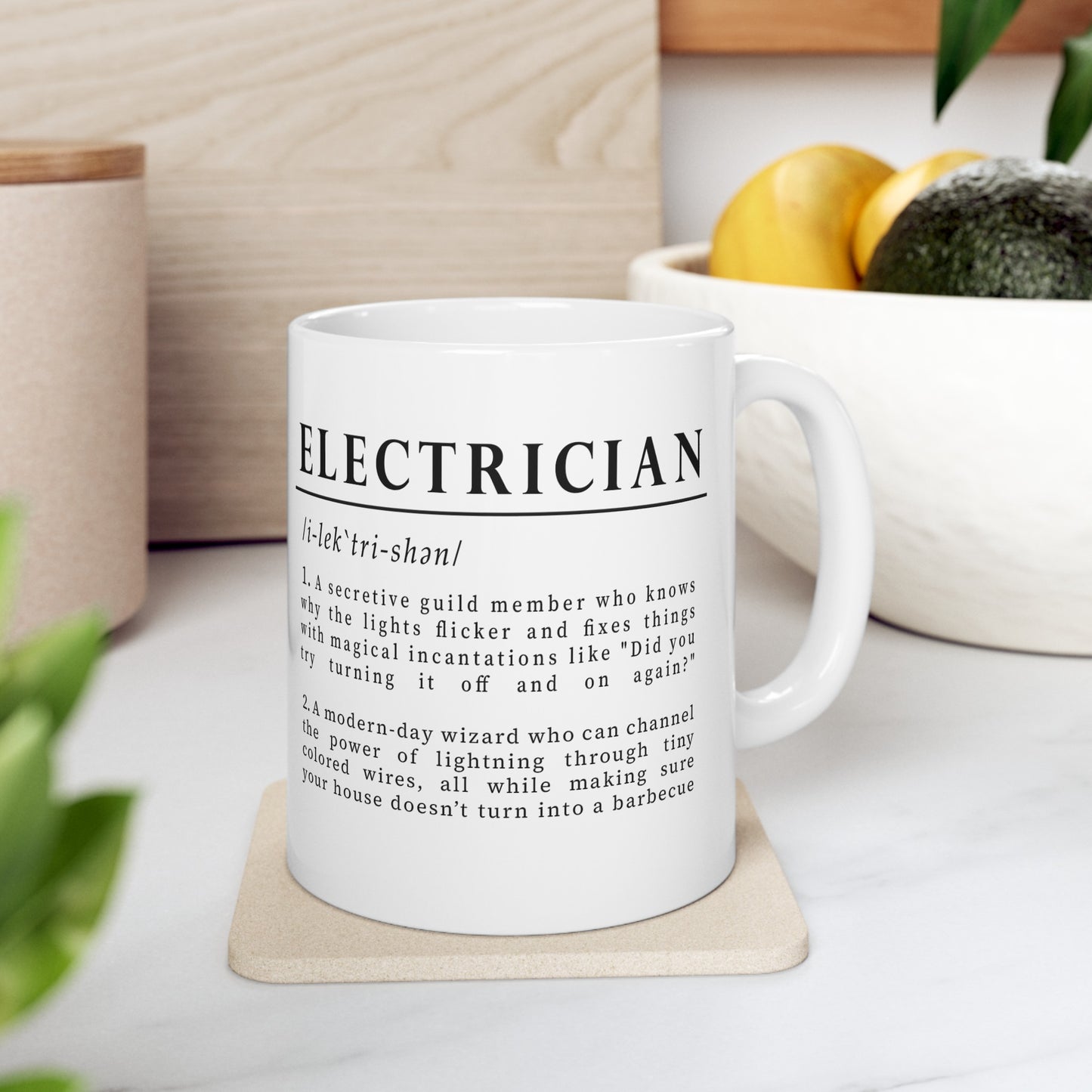 The image shows a white ceramic mug with a humorous definition of 'Electrician' in bold black font. The text describes an electrician as both a secretive guild member and a modern-day wizard of electricity, adding a playful twist to the profession. 