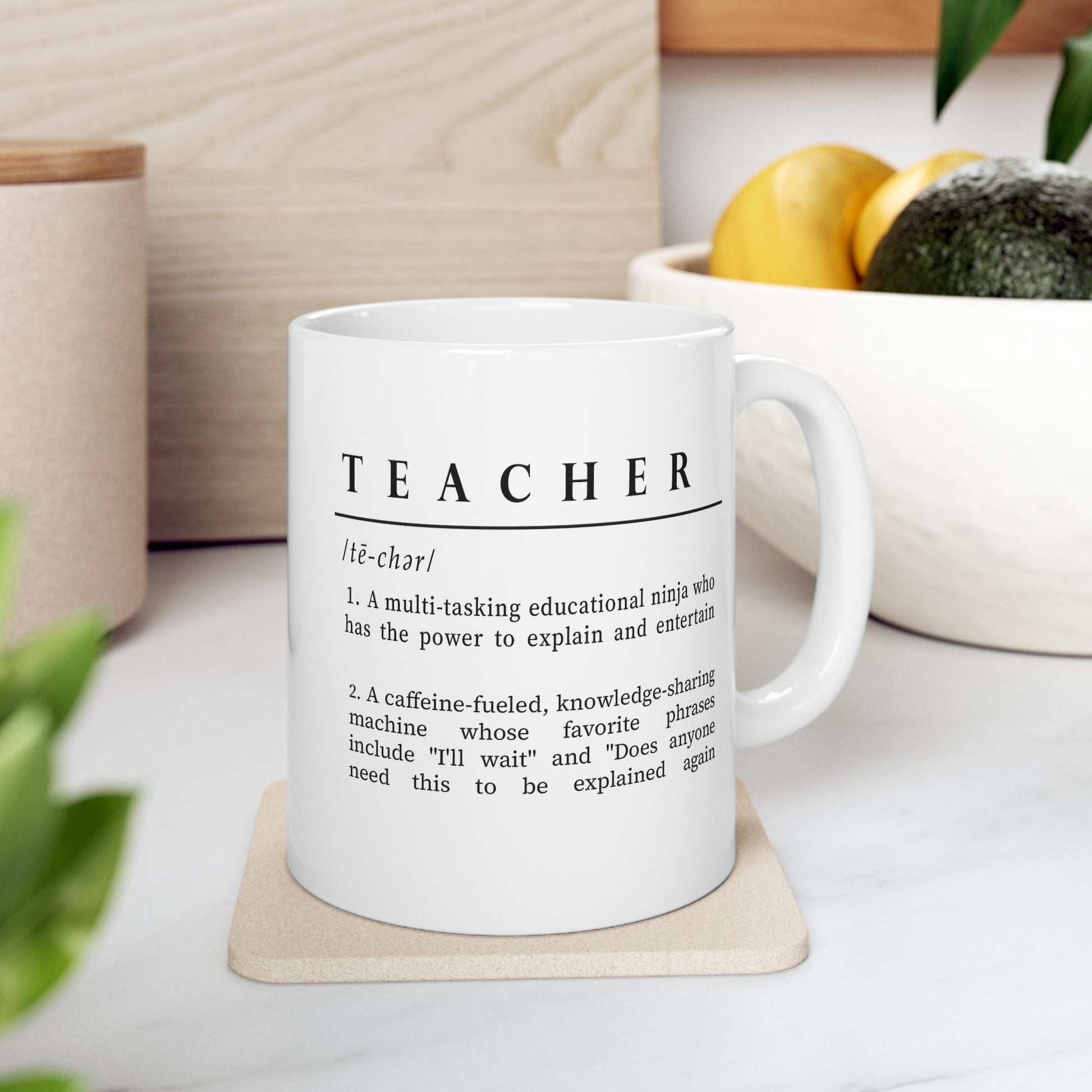 Featured is a white ceramic mug adorned with a clever and affectionate definition of 'Teacher' in black text. The description playfully outlines a teacher as a multitasking educational ninja and a caffeine-fueled knowledge sharer, adding humor to the daily realities of teaching.