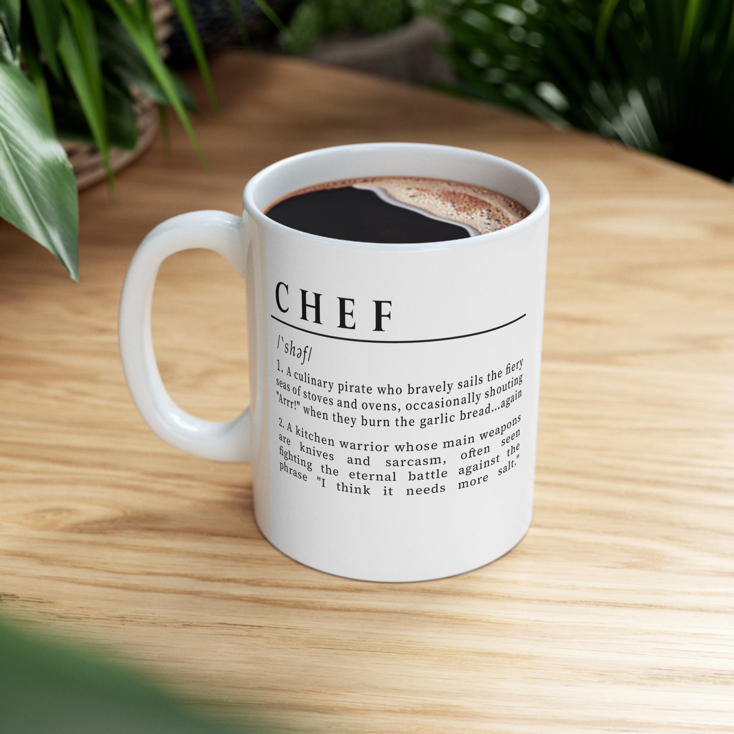 A white ceramic mug with a playful and humorous definition of 'Chef', printed in sharp black lettering. The text describes a chef as a culinary pirate and a kitchen warrior, humorously highlighting the challenges and quirks of culinary life. 