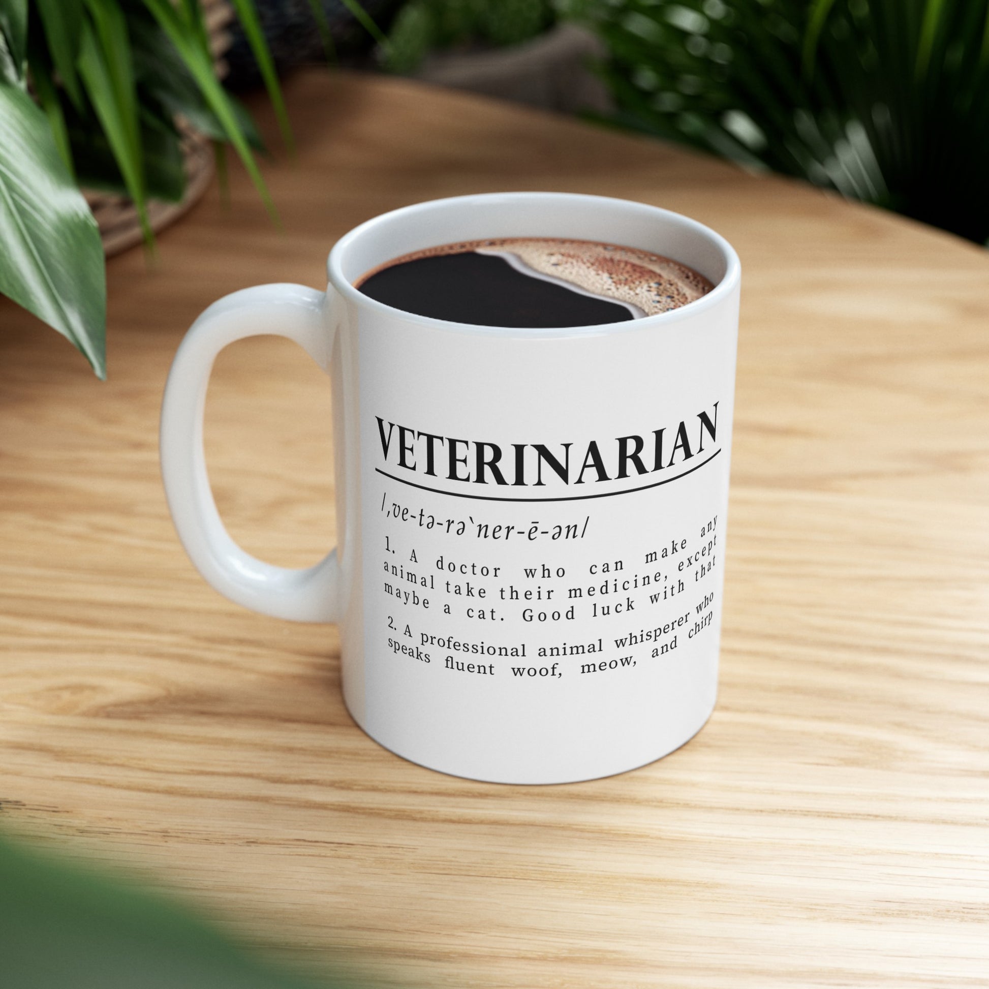 a white cup with bold black text on a plain white background defining 'Veterinarian'. The definition humorously mentions a vet's challenges with medicating animals, especially cats, and describes them as fluent in animal sounds.