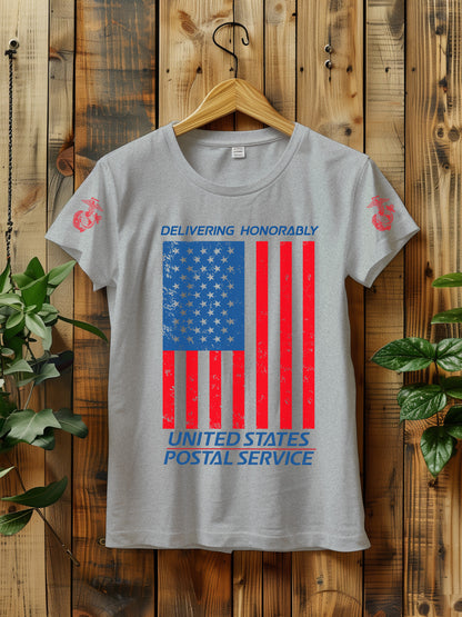 T-shirt hanging on a wooden wall with a hanger, displaying a distressed American flag graphic. The text "Delivering Honorably United States Postal Service" is printed in blue and red. The left sleeve has a red Marine Corps emblem. Two green plants are visible on either side of the shirt.