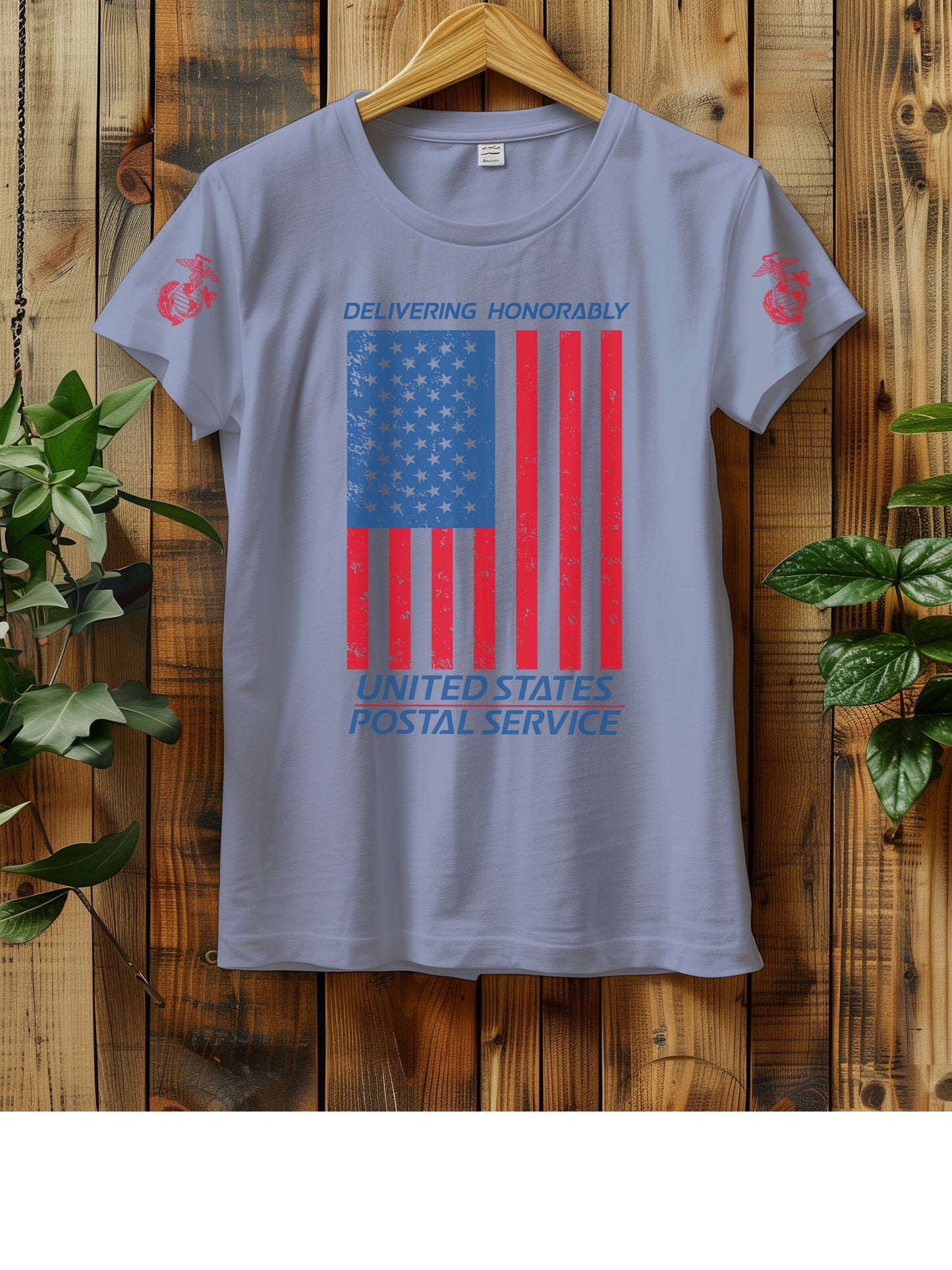 T-shirt hanging on a wooden wall with a hanger, displaying a distressed American flag graphic. The text "Delivering Honorably United States Postal Service" is printed in blue and red. The left sleeve has a red Marine Corps emblem. Two green plants are visible on either side of the shirt.