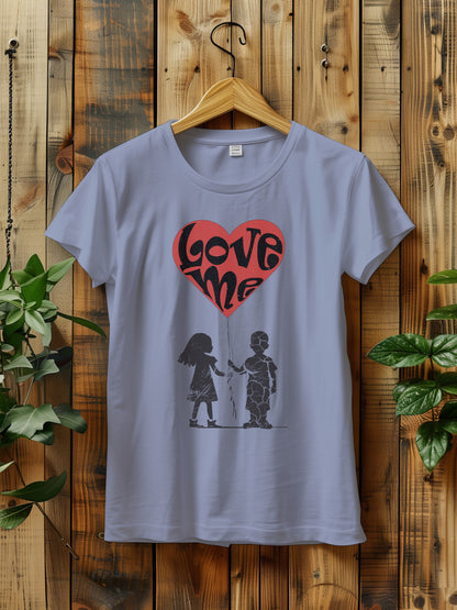 t-shirt hanging on a wooden hanger features a large red heart balloon with love me text, being held by both a a girl and boy