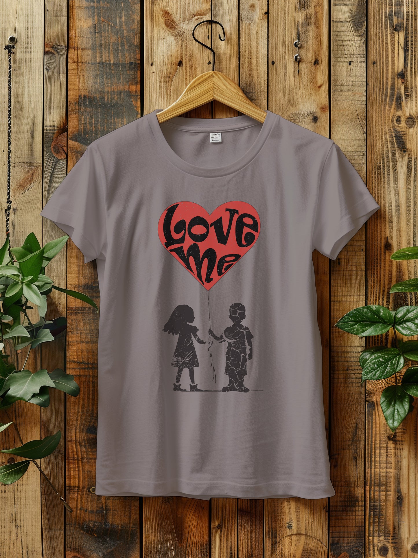 t-shirt hanging on a wooden hanger features a large red heart balloon with love me text, being held by both a a girl and boy