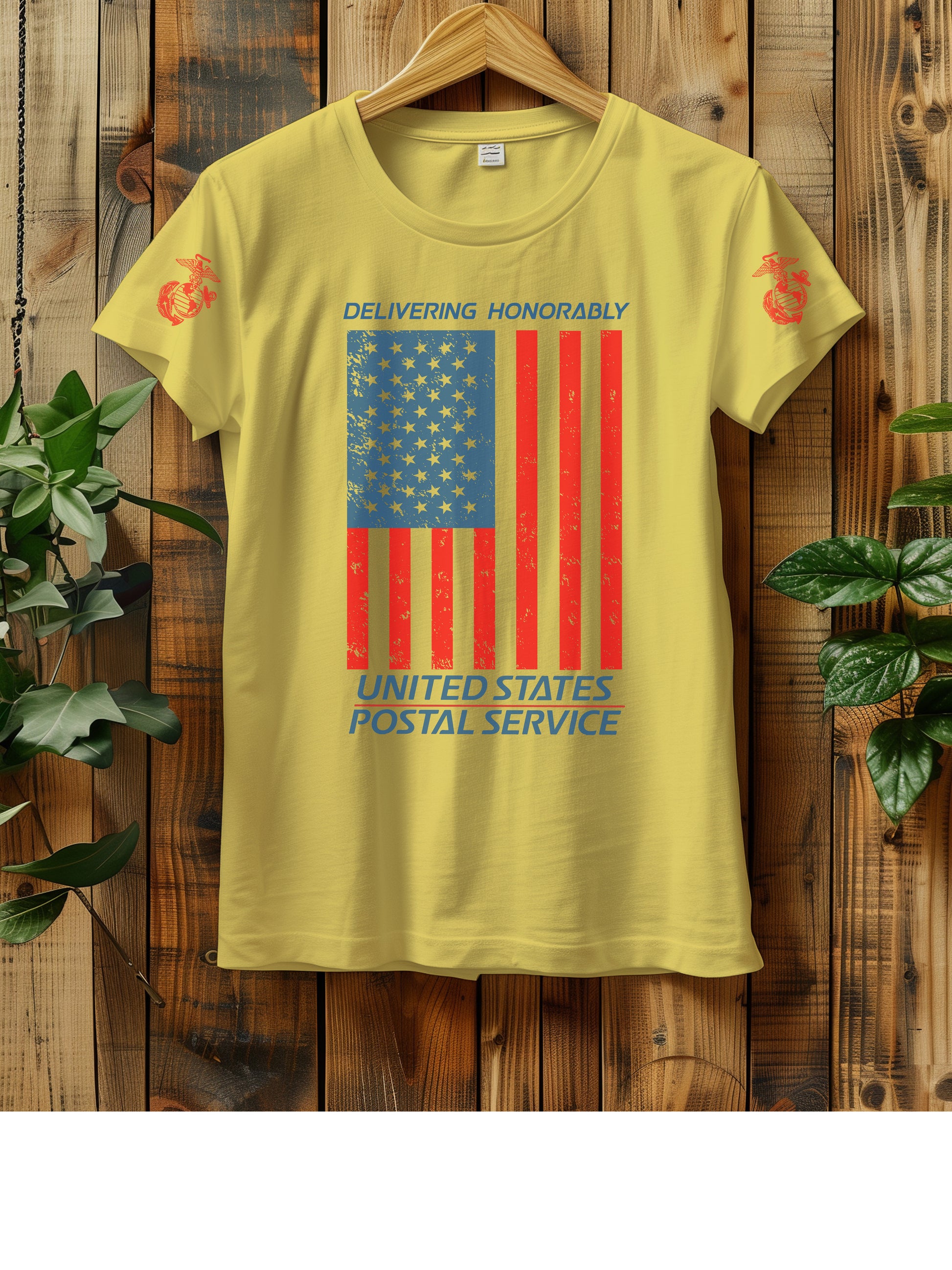 T-shirt hanging on a wooden wall with a hanger, displaying a distressed American flag graphic. The text "Delivering Honorably United States Postal Service" is printed in blue and red. The left sleeve has a red Marine Corps emblem. Two green plants are visible on either side of the shirt.