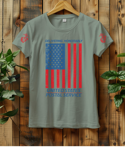 T-shirt hanging on a wooden wall with a hanger, displaying a distressed American flag graphic. The text "Delivering Honorably United States Postal Service" is printed in blue and red. The left sleeve has a red Marine Corps emblem. Two green plants are visible on either side of the shirt.