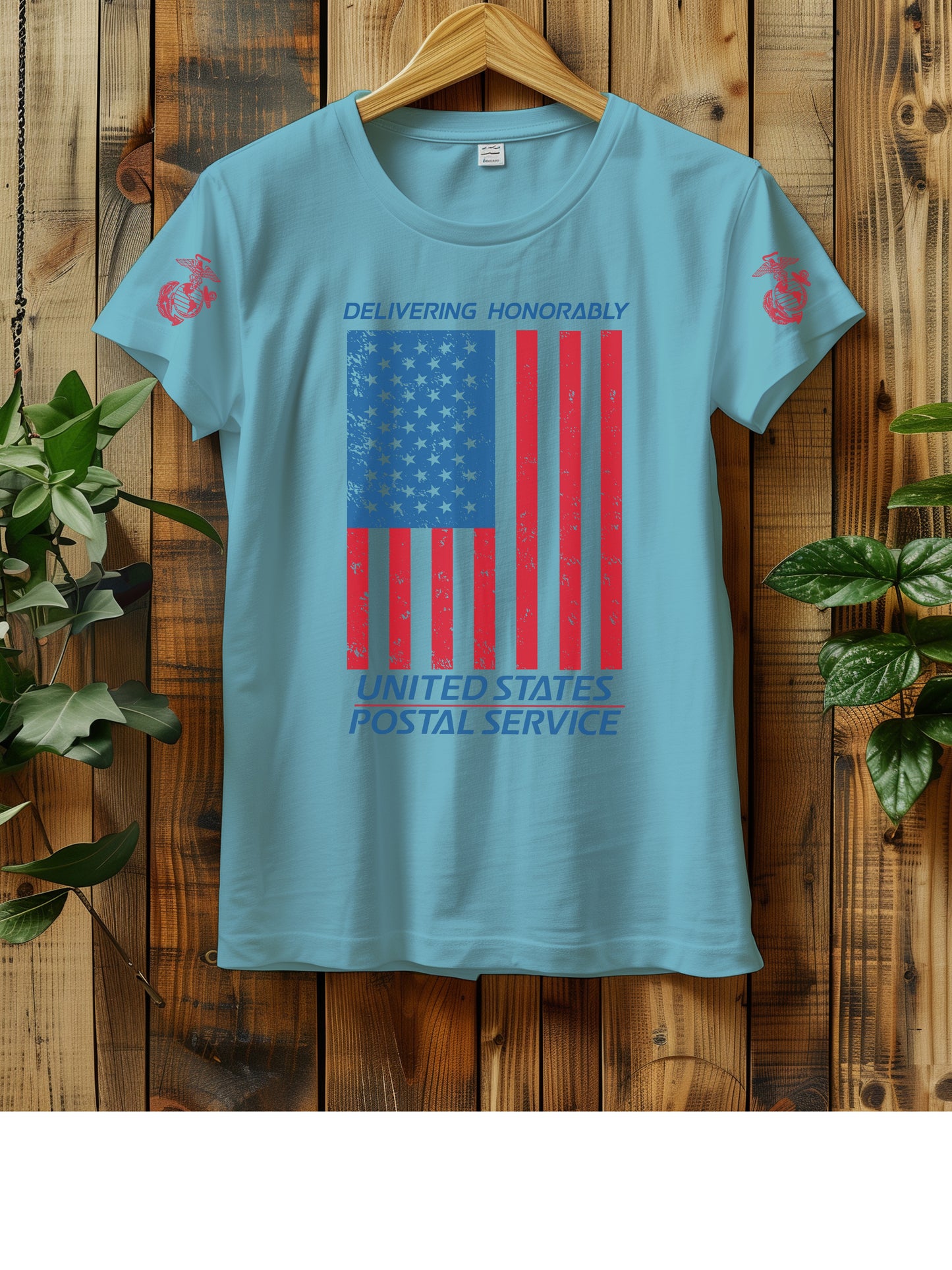 T-shirt hanging on a wooden wall with a hanger, displaying a distressed American flag graphic. The text "Delivering Honorably United States Postal Service" is printed in blue and red. The left sleeve has a red Marine Corps emblem. Two green plants are visible on either side of the shirt.