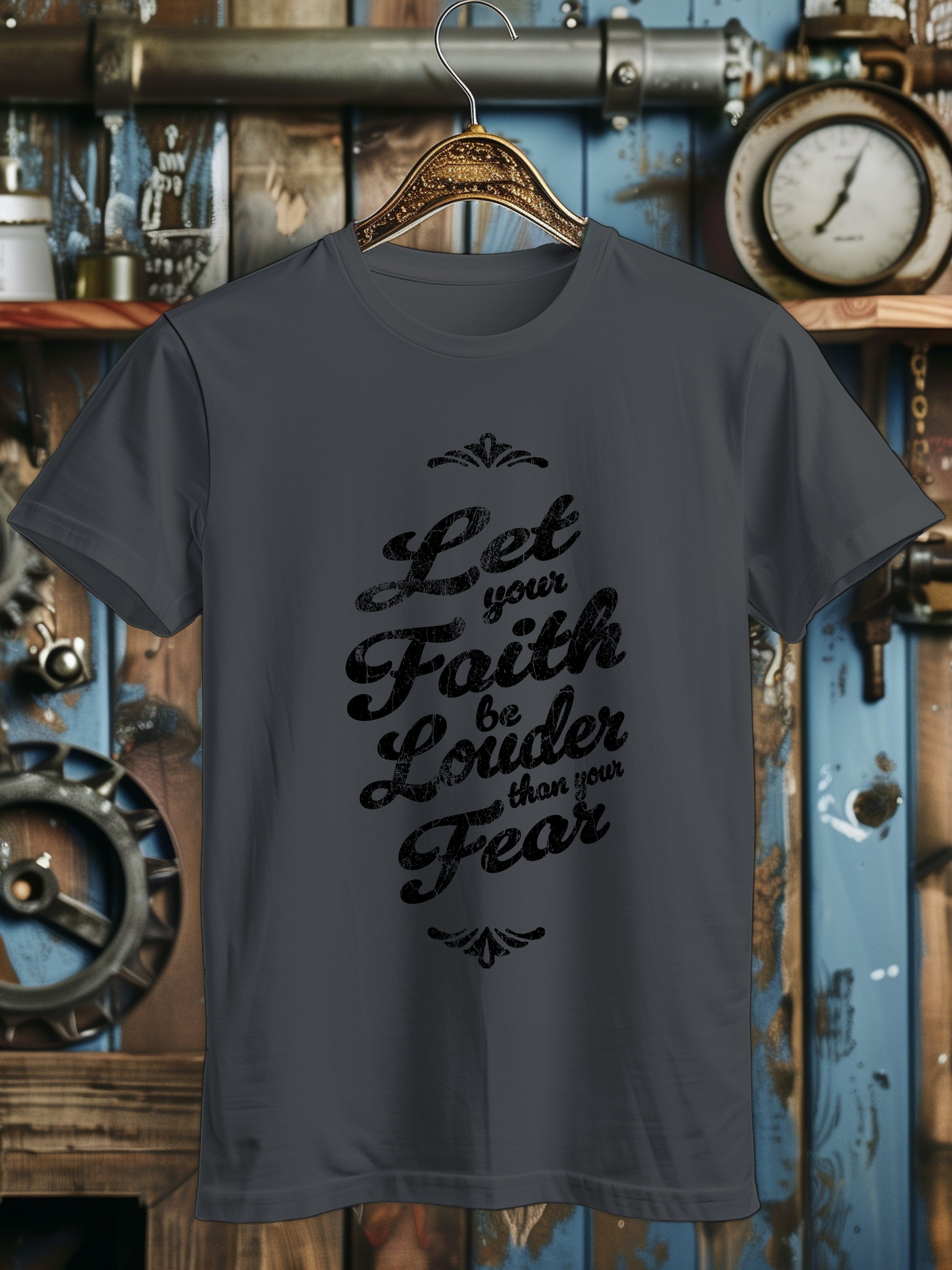 A T-shirt with the phrase Let your Faith be Louder than your Fear in decorative black script, displayed on a wooden hanger.