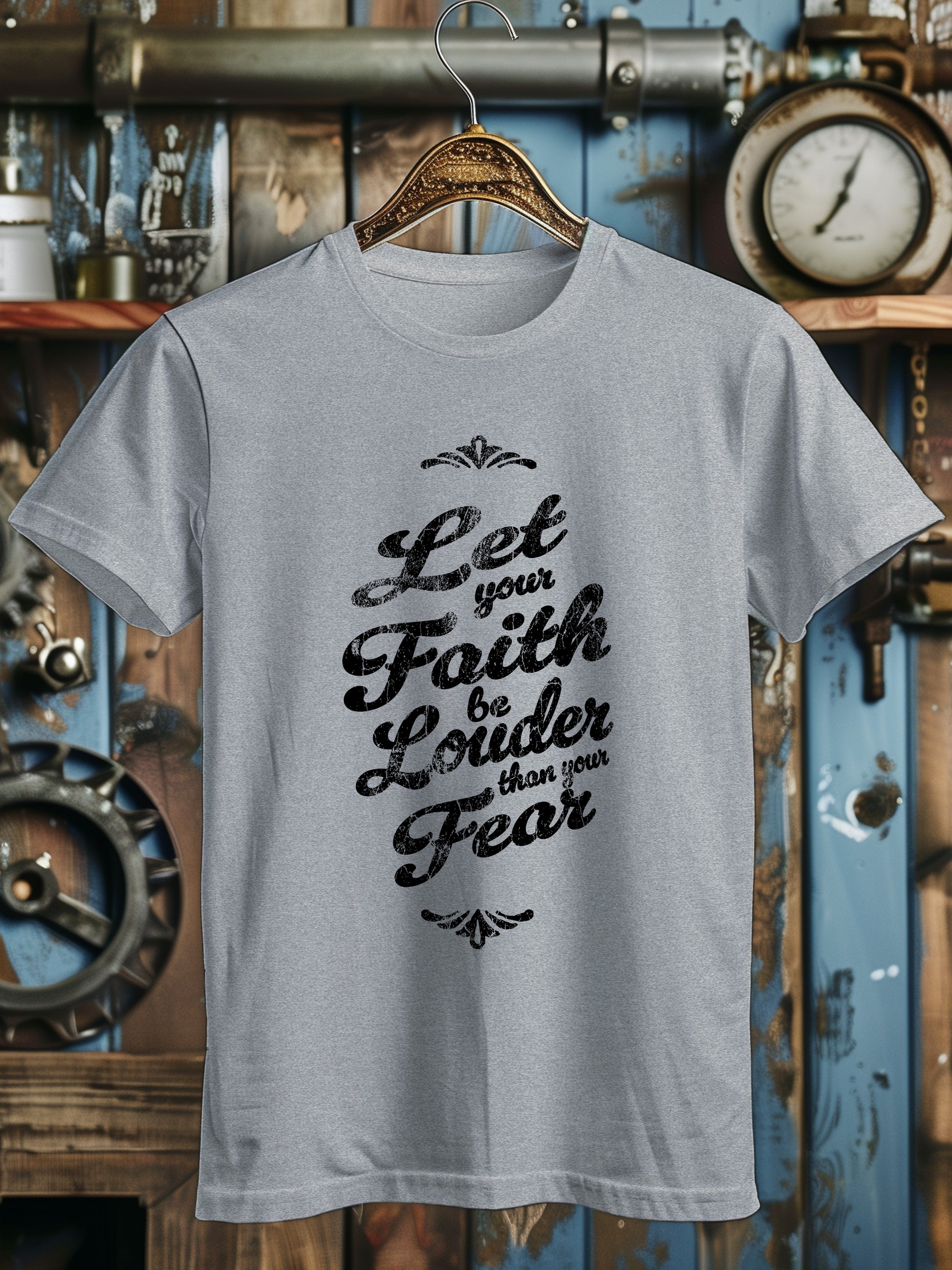 A T-shirt with the phrase Let your Faith be Louder than your Fear in decorative black script, displayed on a wooden hanger.