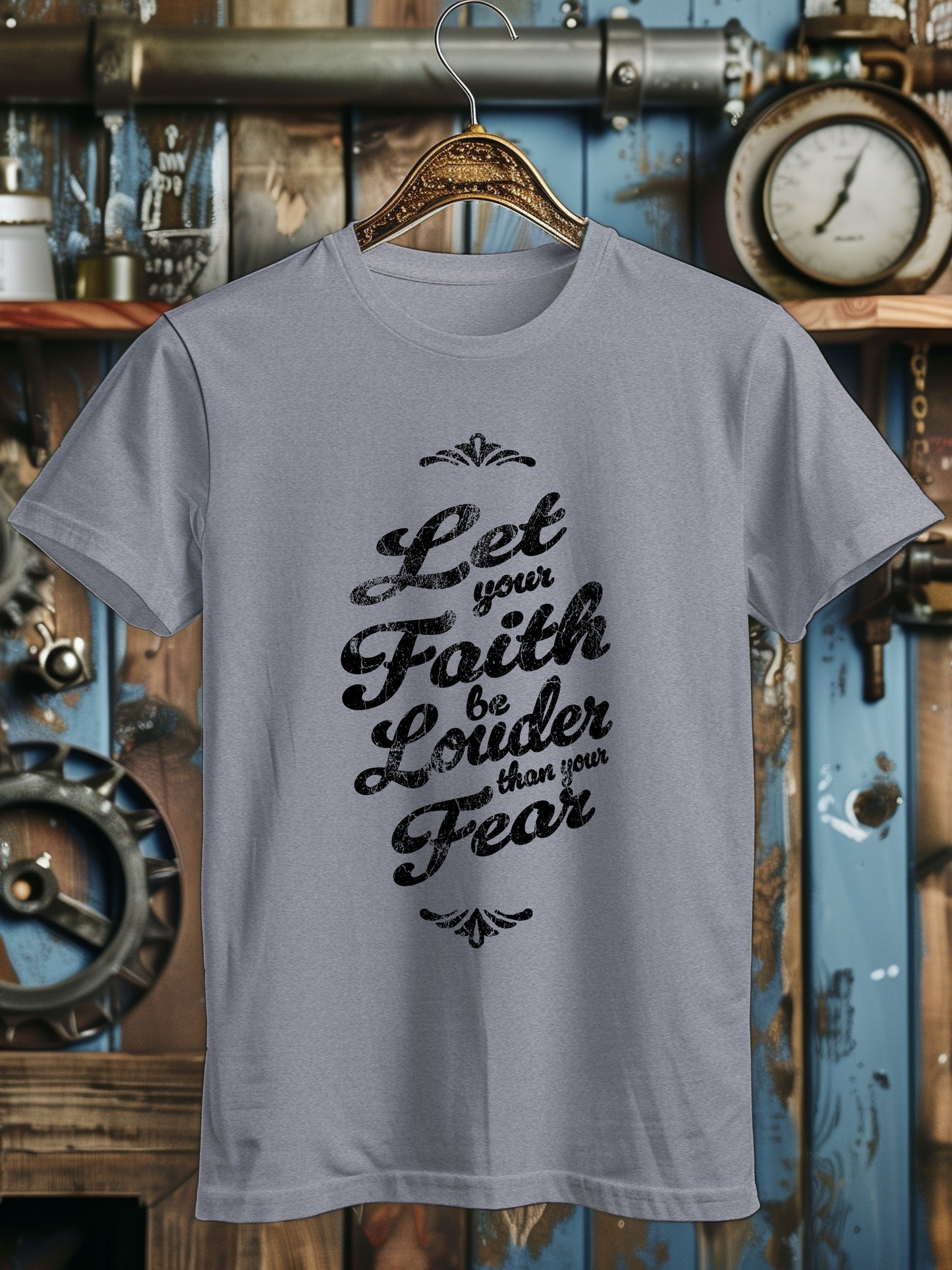 A T-shirt with the phrase Let your Faith be Louder than your Fear in decorative black script, displayed on a wooden hanger.