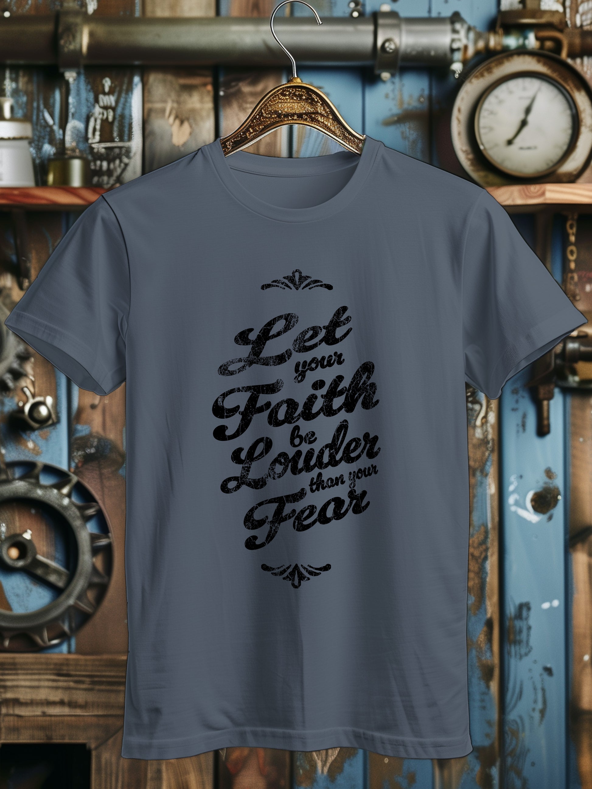 A T-shirt with the phrase Let your Faith be Louder than your Fear in decorative black script, displayed on a wooden hanger.