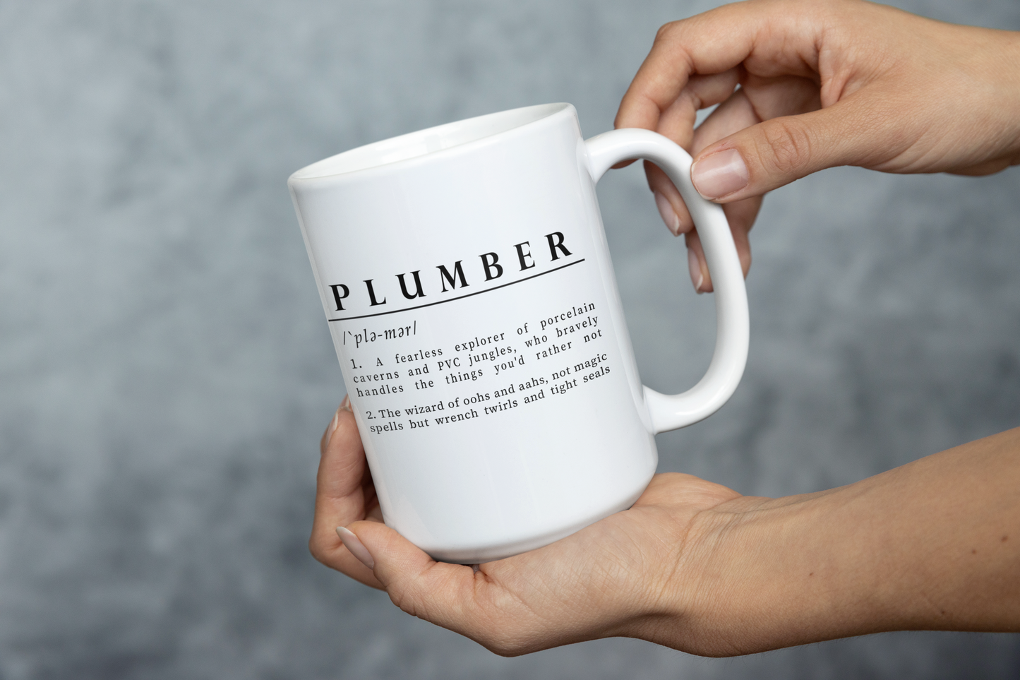 white ceramic mug with a witty definition of 'Plumber' printed in black. The humorous description highlights a plumber as both an explorer of pipes and a skilled artisan.