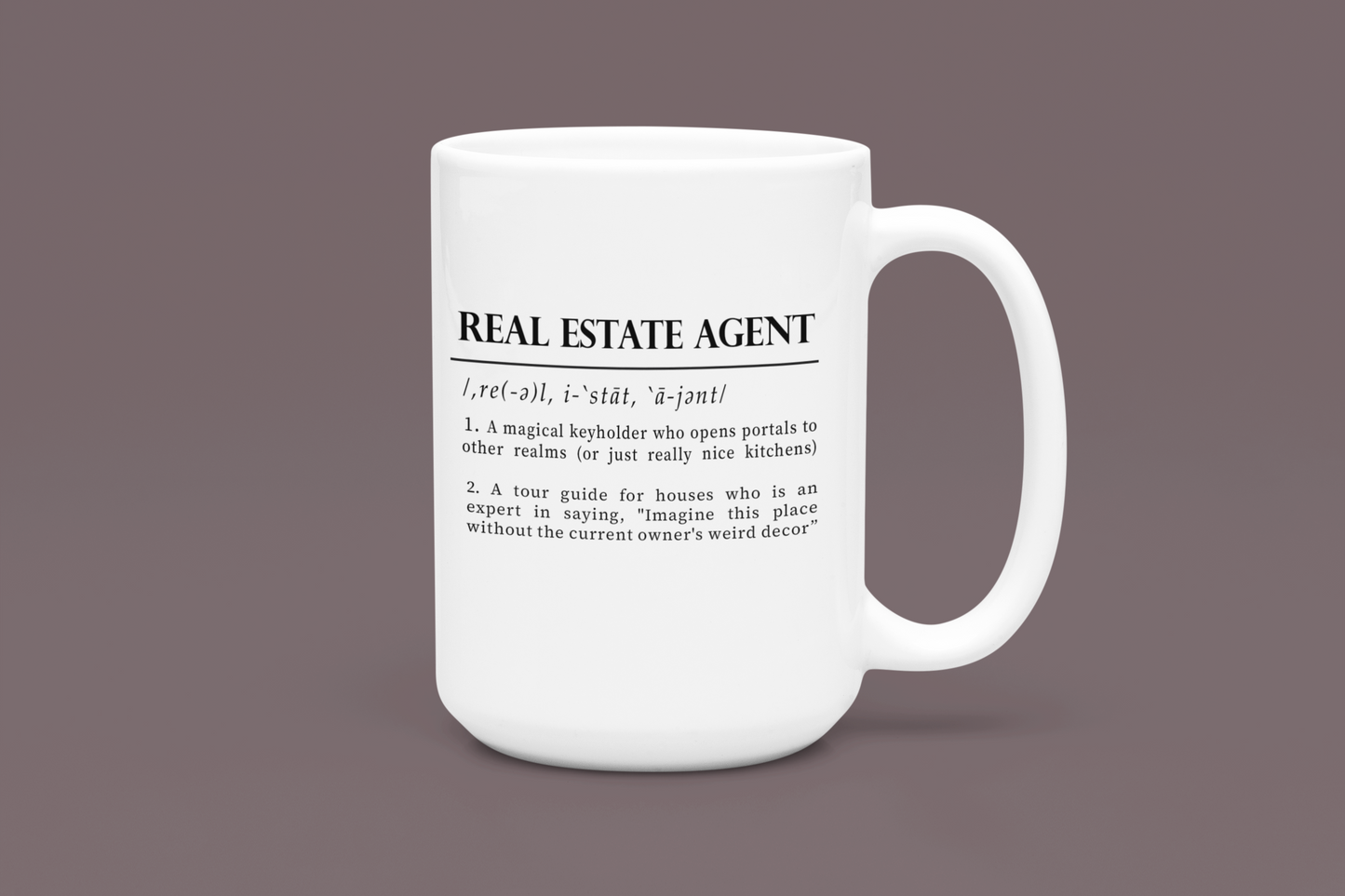 A classic white ceramic mug features a playful definition of 'Real Estate Agent' printed in elegant black font. The text humorously describes the agent as a keyholder to realms and an expert in home decor imagination. 