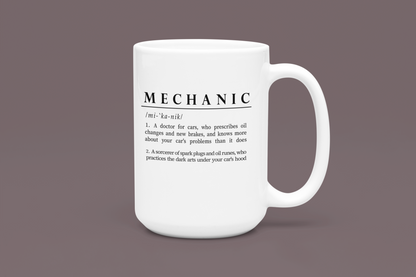 Displayed is a white ceramic mug with a witty definition of 'Mechanic' in bold black font. The text creatively describes a mechanic as both a car doctor and a sorcerer of automotive parts, adding a humorous and mythical element to the profession. 