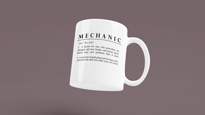 Displayed is a white ceramic mug with a witty definition of 'Mechanic' in bold black font. The text creatively describes a mechanic as both a car doctor and a sorcerer of automotive parts, adding a humorous and mythical element to the profession. 