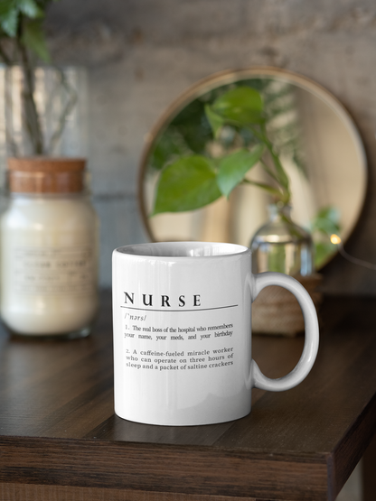 A white ceramic mug features a playful definition of 'Nurse' in black font. The humorous description portrays a nurse as both the caring boss of the hospital and a caffeine-powered miracle worker, highlighting their dedication and resilience.